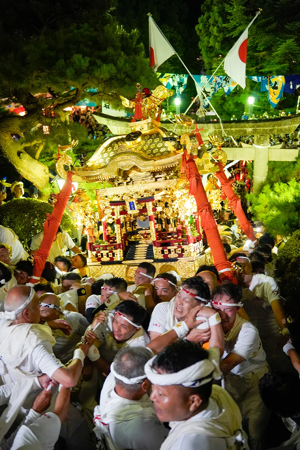 山田祭りの夜、鳥居の下で金色の神輿を担ぎ揉み合う白装束の男たち
