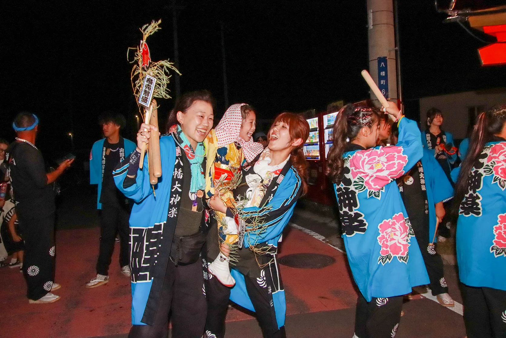 山田祭りの夜、縁起物を手に笑顔で盛り上がる八幡大神楽の担い手たち