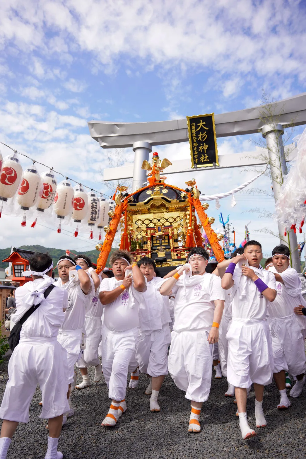 大杉神社の鳥居をくぐり金色の神輿を担いで進む白装束の担ぎ手たち